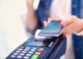 Mano que acerca un celular a una terminal de pago POS con teclado para pagar sin contacto